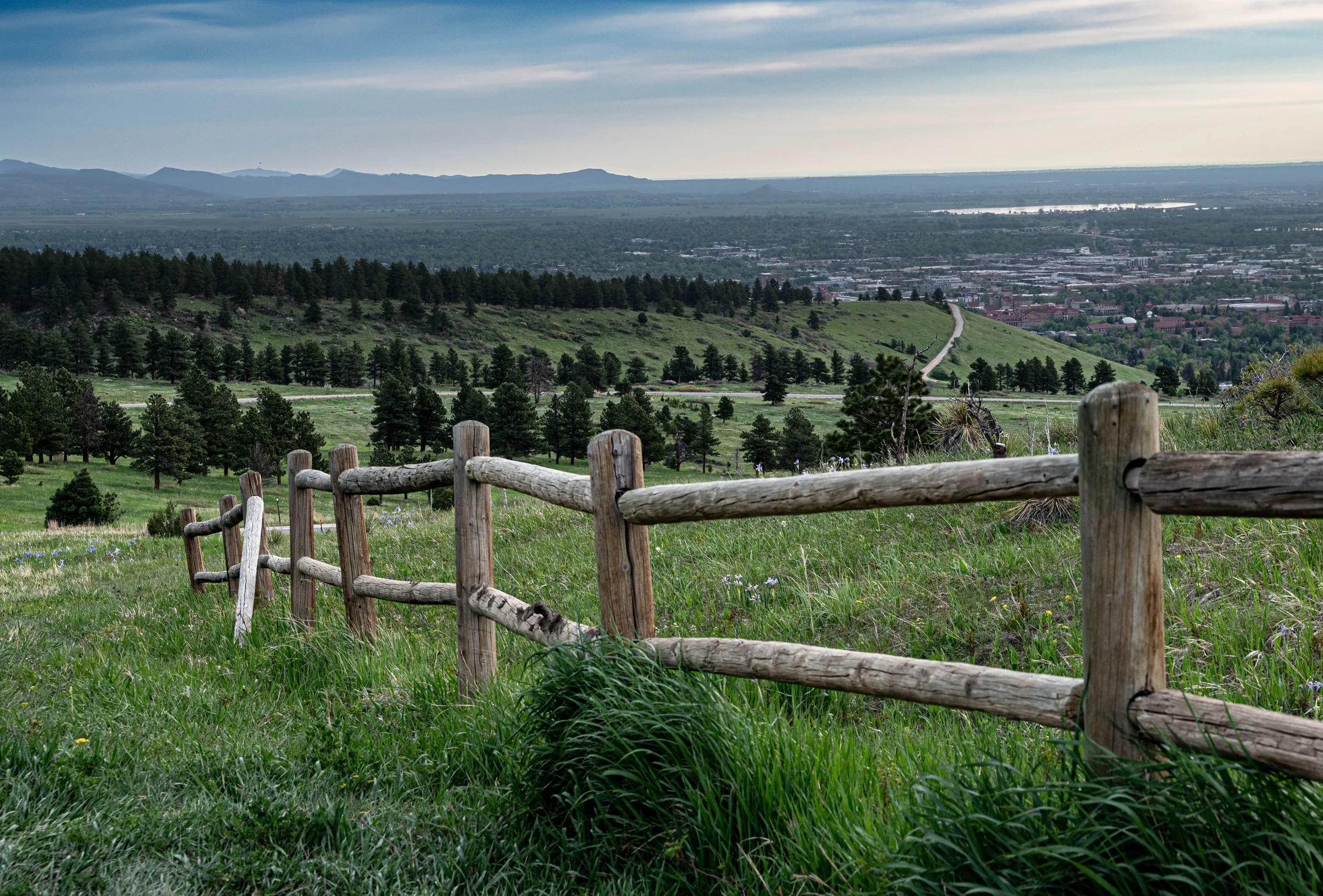 A wooden rail fence on green foothill pasture, looking out over the plains of the Front Range