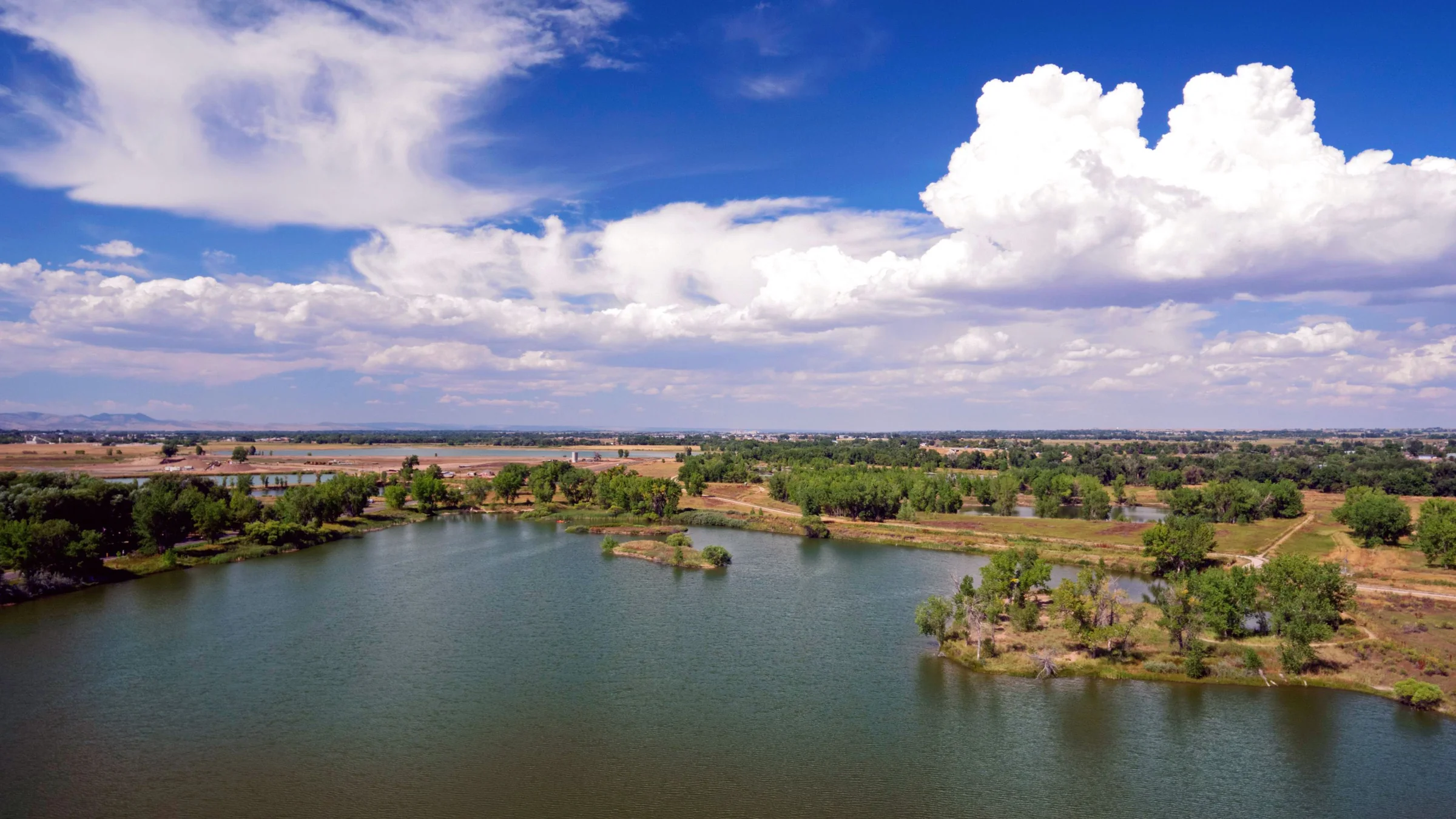 A lake with cottonwoods under tall clouds on the plains near Fort Collins